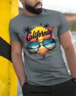 California Beach Vibes Tee Retro Sunset Sunglasses T-Shirt for West Coast Fans - model in grey shirt leaning against column