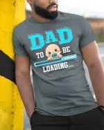 Dad To Be Loading Funny Pregnancy T-Shirt - model in grey shirt leaning against column