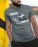 I Believe I Can Fly Funny Bike Crash T-Shirt for Cyclists - model in grey shirt leaning against column