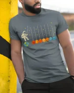 Astronaut Swinging on Planets Funny Space T-Shirt for Adults - model in grey shirt leaning against column