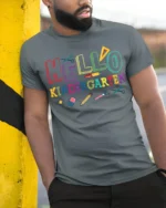 Hello Kindergarten Rainbow School Supplies T-Shirt - model in grey shirt leaning against column