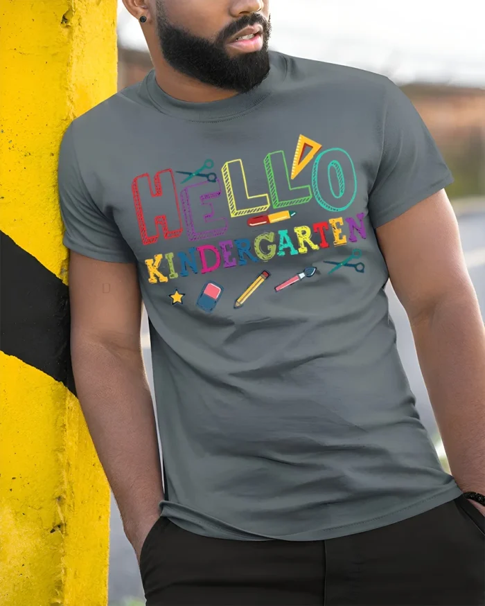 Hello Kindergarten Rainbow School Supplies T-Shirt - model in grey shirt leaning against column
