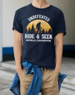 Undefeated Hide And Seek World Champion Bigfoot Funny Sasquatch T Shirt - model wearing navy tee with hands in pockets