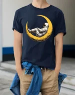 Dreaming Astronaut Resting On Moon Space Art Graphic T Shirt - model wearing navy tee with hands in pockets