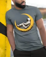 Dreaming Astronaut Resting On Moon Space Art Graphic T Shirt - model wearing grey tee, leaning on column