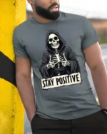 Funny Stay Positive Skeleton Thumbs Up Graphic T Shirt - model wearing grey tee, leaning on column