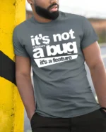 Funny Its Not A Bug Its A Feature Programmer Humor T Shirt - model wearing grey tee, leaning on column