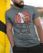 Funny Broken Brain On Crutches Graphic T Shirt Mental Humor Tee - model wearing grey tee, leaning on column