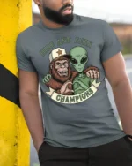 Hide And Seek Champions Funny Alien Bigfoot Graphic T Shirt Style - model wearing grey tee, leaning on column