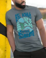 Be Kind To The Sea Graphic Tshirt Ocean Lover Coastal Style - model wearing grey tee, leaning on column