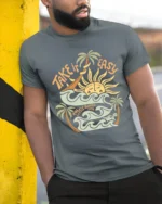 Take It Easy Retro Surf Beach Sunset Graphic Tee Tshirt - model wearing grey tee, leaning on column