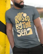 Raised By The Sea Beach Lover Graphic Tee Coastal Style - model wearing grey tee, leaning on column