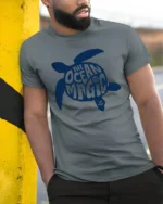 The Ocean Is Magic Sea Turtle Graphic Tee Coastal Style - model wearing grey tee, leaning on column
