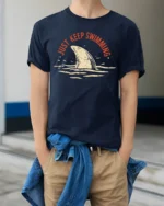 Just Keep Swimming Shark Graphic Tee Funny Ocean Style - model wearing navy tee with hands in pockets