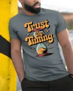 Trust The Timing Retro Hourglass Motivational Graphic Tee - model wearing grey tee, leaning on column