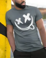 Edgy Smiley Face X Eyes Tongue Out Cool Graphic Tee - model wearing grey tee, leaning on column