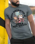 Easily Distracted By Cats And Side Quests Funny Gamer T Shirt - model wearing grey tee, leaning on column