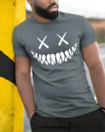 Creepy Smile Skull Face X Eyes Minimalist Graphic T Shirt - model wearing grey tee, leaning on column