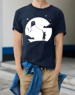 Boy Flying Kite Moonlight Silhouette Graphic T Shirt Dreamy Tee - model wearing navy tee with hands in pockets
