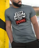 Motivational Stop Dreaming Start Doing Graphic Tshirt - model wearing grey tee, leaning on column