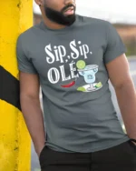 Festive Sip Sip Ole Margarita Cocktail Slogan Graphic Tee - model wearing grey tee, leaning on column