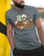 Skeleton Office Overwork Keep Working No Time To Die Tshirt - model wearing grey tee, leaning on column
