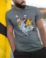 Skeleton Surfer Riding Shark Tropical Sunset Graphic Tee - model wearing grey tee, leaning on column