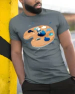 Creative Artistic Astronaut Painter Space Palette Graphic Tshirt - model wearing grey tee, leaning on column