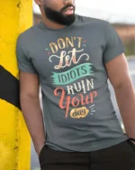 Don’t Let Idiots Ruin Your Day Graphic Tee - model wearing grey tee, leaning on column