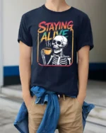 Staying Alive Skeleton Coffee Drinking Graphic Tee - model wearing navy tee with hands in pockets