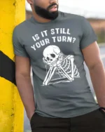 Relatable Is It Still Your Turn Board Game Skeleton Graphic Tee - model wearing grey tee, leaning on column