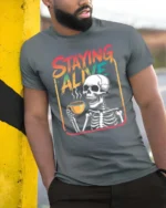 Staying Alive Skeleton Coffee Drinking Graphic Tee - model wearing grey tee, leaning on column