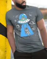 Creative Alien Spaceship Astronaut Swing Cosmic Graphic Tee - model wearing grey tee, leaning on column