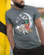 Captivating Astronaut Alien Moon Pizza Box Graphic Tee - model wearing grey tee, leaning on column