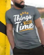 Inspiring Good Things Take Time Positive Graphic Tshirt - model wearing grey tee, leaning on column