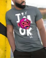 Gritty Pink Monkey Im Ok Broken Cartoon Graphic Tshirt - model wearing grey tee, leaning on column