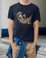 Sarcastic Bone Tired Sleeping Skeleton Hammock Graphic Tee - model wearing navy tee with hands in pockets