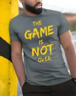Ultimate The Game Is Not Over Yellow Typography Tshirt - model wearing grey tee, leaning on column