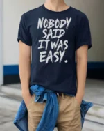 Striking Nobody Said It Was Easy Grit Motivation Graphic Tee - model wearing navy tee with hands in pockets