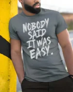 Striking Nobody Said It Was Easy Grit Motivation Graphic Tee - model wearing grey tee, leaning on column